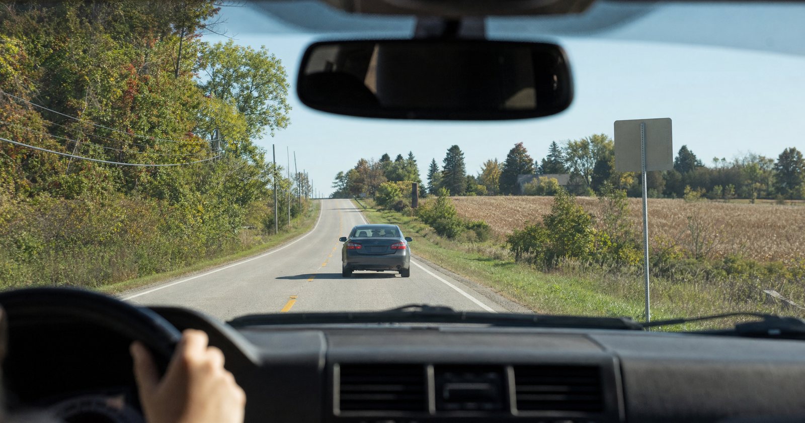 A driver’s view of a car well ahead on a two-lane country road.