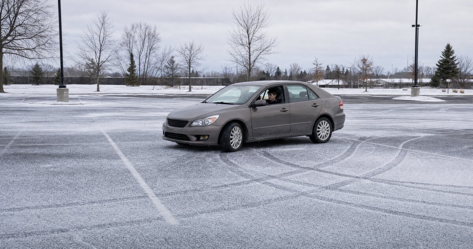 A car sliding sideways across an empty, snow-covered parking lot.
