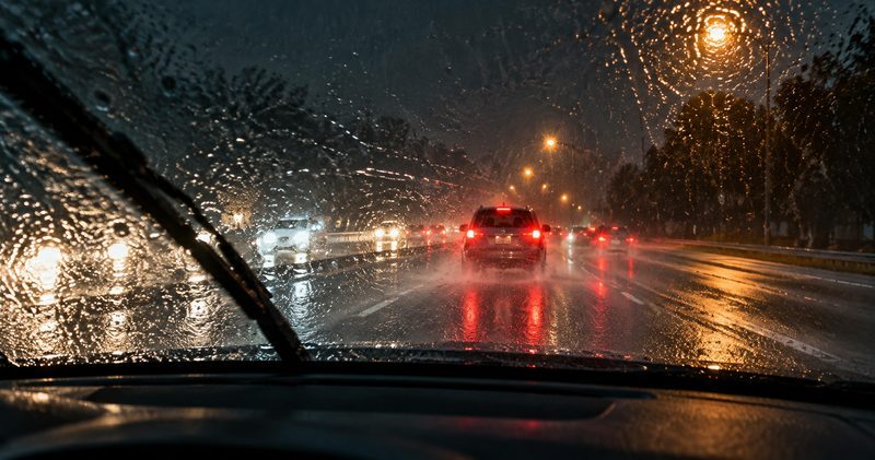 Heavy rain on a windshield at night, with taillights on the wet highway ahead.